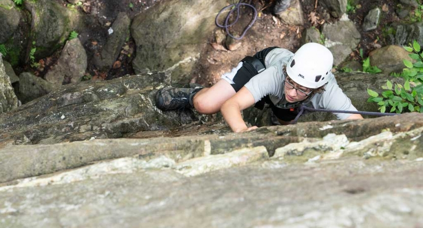 From above, you can see a rock climber wearing safety gear making their way up a rock wall